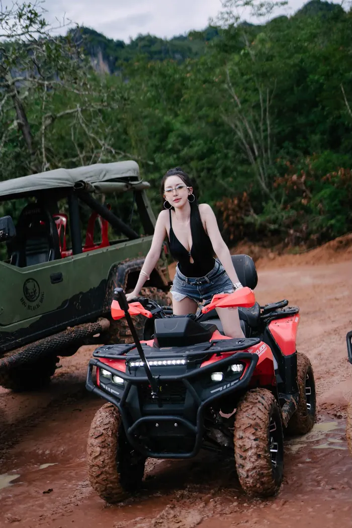 ลูกค้านั่งถ่ายรูปบนรถ ATV สีแดงที่เปื้อนโคลน มีรถบักกี้จอดอยู่ด้านหลัง